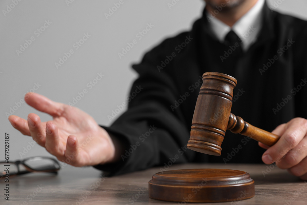 Judge with gavel sitting at wooden table against light grey background, closeup Judge with gavel sitting at wooden table against light grey background, closeup