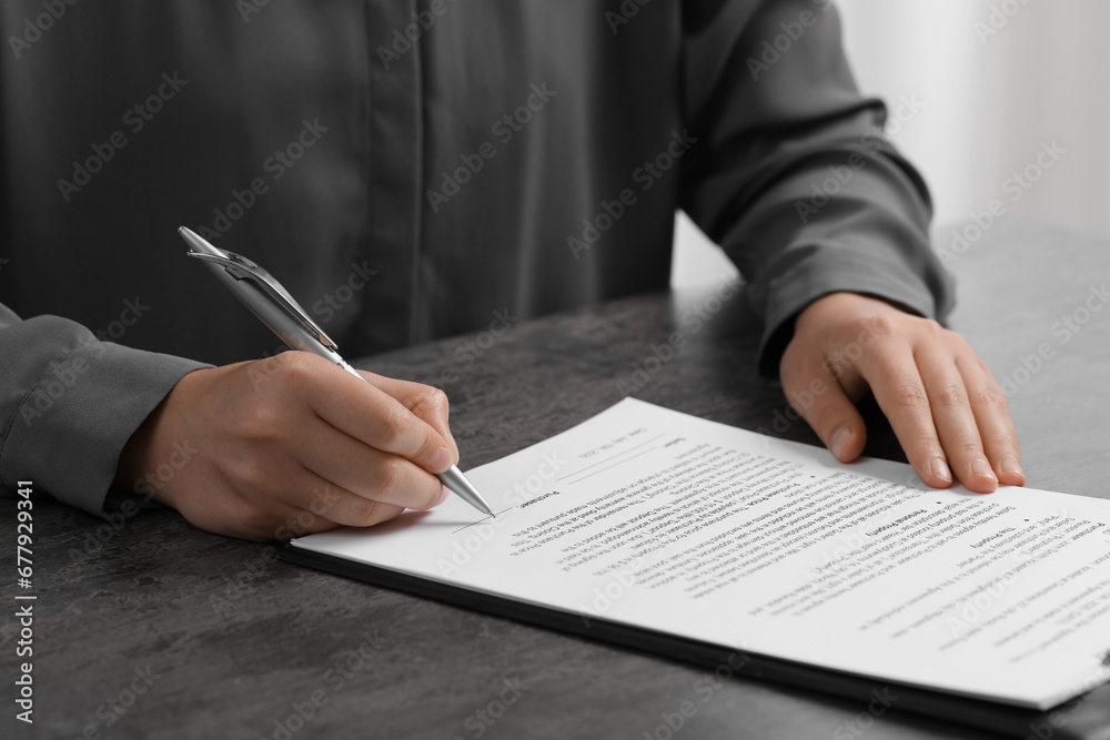 Woman signing document at dark table indoors, closeup Woman signing document at dark table indoors, closeup
