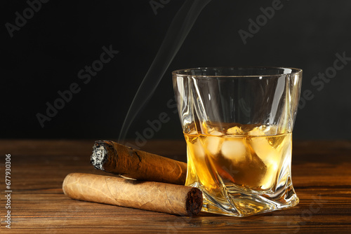 Glass of whiskey with ice cubes and cigars on wooden table