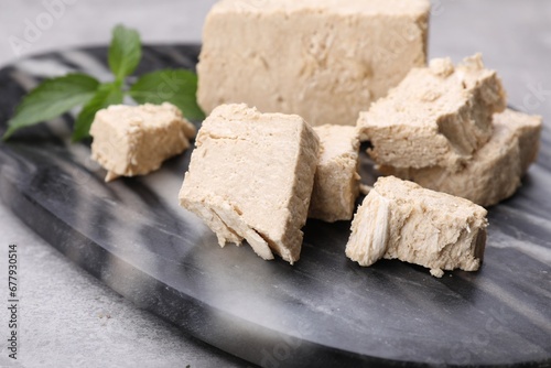 Pieces of tasty halva and mint served on light grey table, closeup