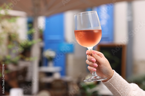 Woman holding glass of rose wine outdoors, closeup. Space for text