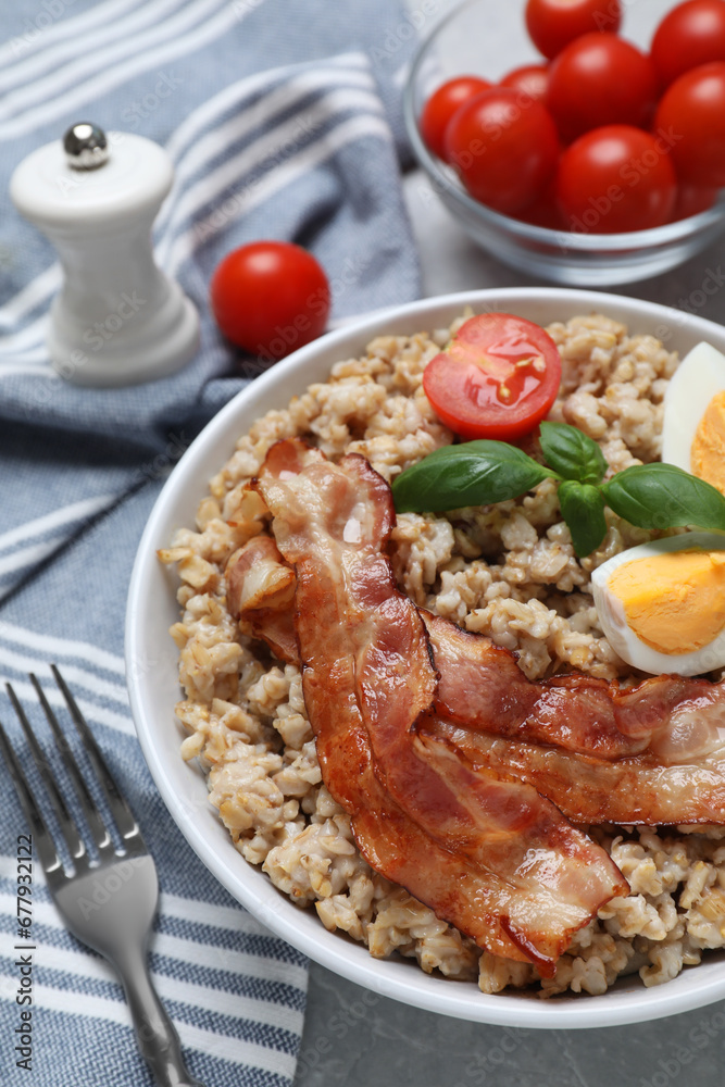 Tasty boiled oatmeal with egg, bacon and tomatoes served on light grey table, closeup Tasty boiled oatmeal with egg, bacon and tomatoes served on light grey table, closeup
