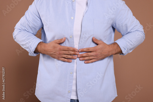 Man suffering from stomach pain on light brown background, closeup