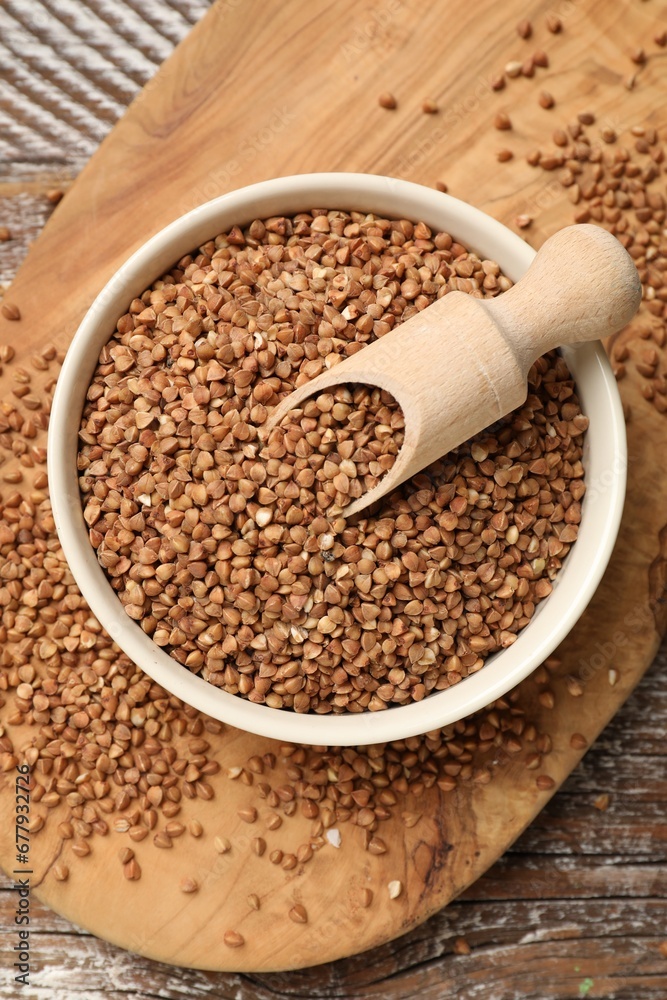 Bowl and scoop with dry buckwheat on wooden table, top view Bowl and scoop with dry buckwheat on wooden table, top view