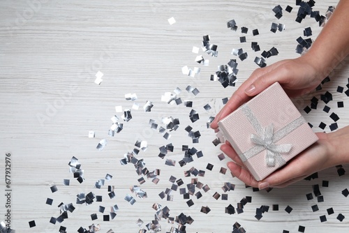 Christmas present. Woman with gift box and confetti on white wooden background, top view. Space for text