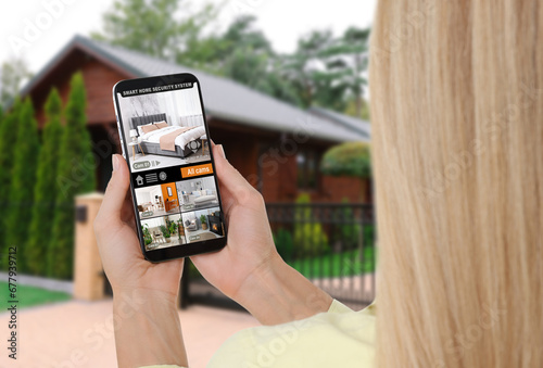 Woman using smart home security system on mobile phone near house outdoors. Device showing different rooms through cameras