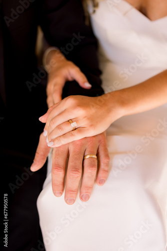 Bride and groom are sitting together with their hands together showing off their wedding bands. 