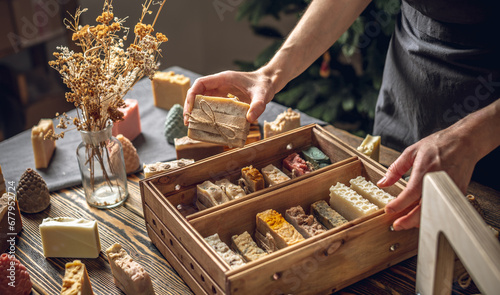 A woman soap maker holds handmade soap in her hands. A lot of different sliced pieces in a wooden box. Eco-friendly natural handmade cosmetics
