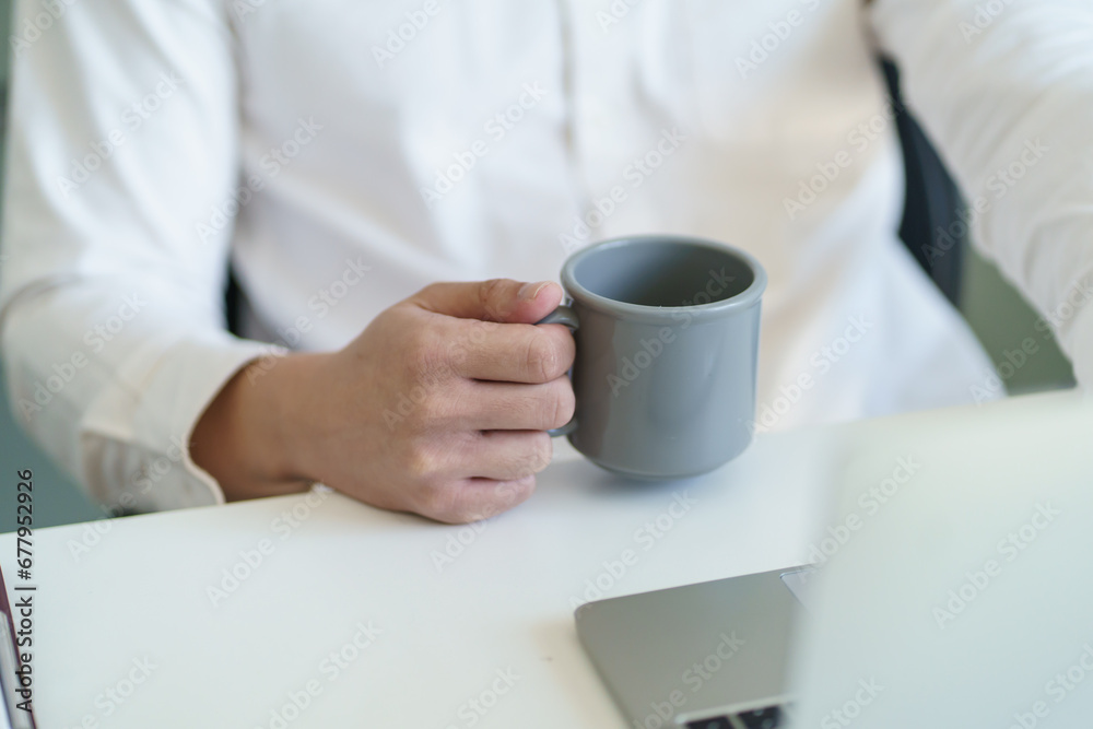 Happy Young business man. drinking coffee and working on laptop computer while sitting at office Happy Young business man. drinking coffee and working on laptop computer while sitting at office