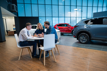 Happy caucasian couple signs a contract for the purchase of a car salon.