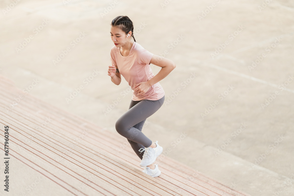 Fototapeta premium Full length sporty young Asian woman running on steps. Young female in sportswear jogging while exercising on the steps outdoor.