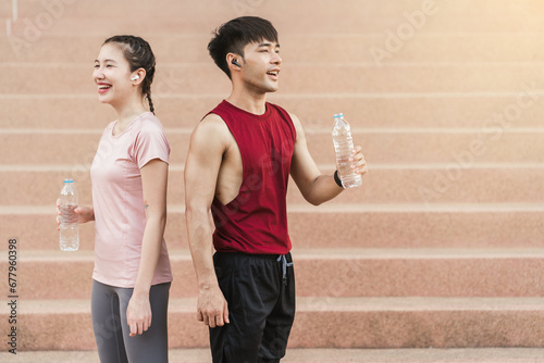 Young Asian couple athlete drinking water after exercising outdoors in park. Drinking water from bottle, Healthy exercise concept.