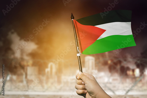 Closeup of a man holds a Palestinian flag in front of a burning city photo