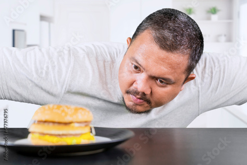 Middle aged overweight man looking at a cheeseburger thinking of eating it at home