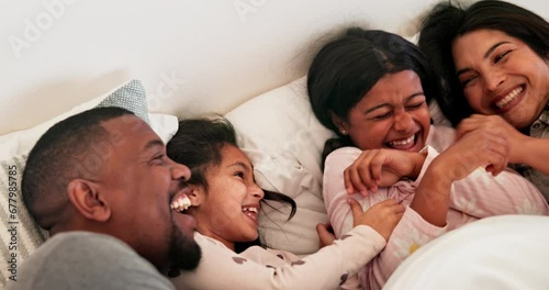 Funny, family and children in bedroom, tickle and play, bonding and happy together in the morning in home. Laughing kids, mother and father in bed, smile and care of interracial parents in top view photo