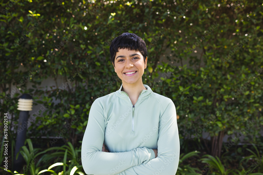 Portrait of happy biracial woman with short dark hair crossing arms and smiling in sunny garden Portrait of happy biracial woman with short dark hair crossing arms and smiling in sunny garden