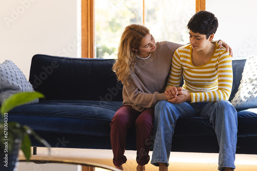 Sad biracial lesbian couple embracing and comforting, on couch in sunny living room, copy space