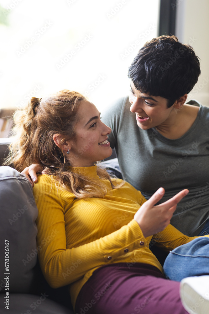 Happy biracial lesbian couple embracing on couch and talking in sunny living room Happy biracial lesbian couple embracing on couch and talking in sunny living room