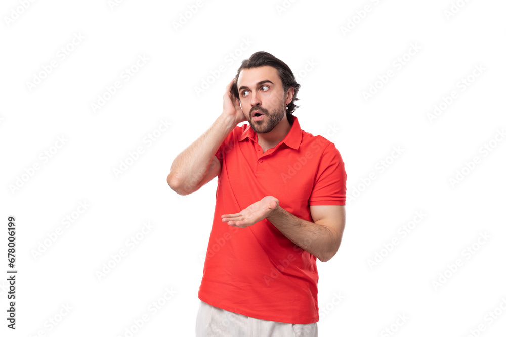young handsome man with black hair and beard dressed in a red t-shirt throws up his hands using a smartphone young handsome man with black hair and beard dressed in a red t-shirt throws up his hands using a smartphone