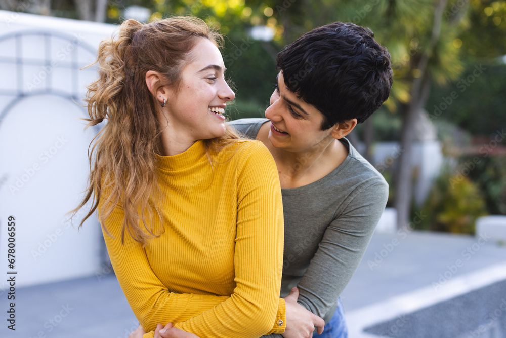 Happy biracial lesbian couple standing on garden terrace embracing and smiling at each other