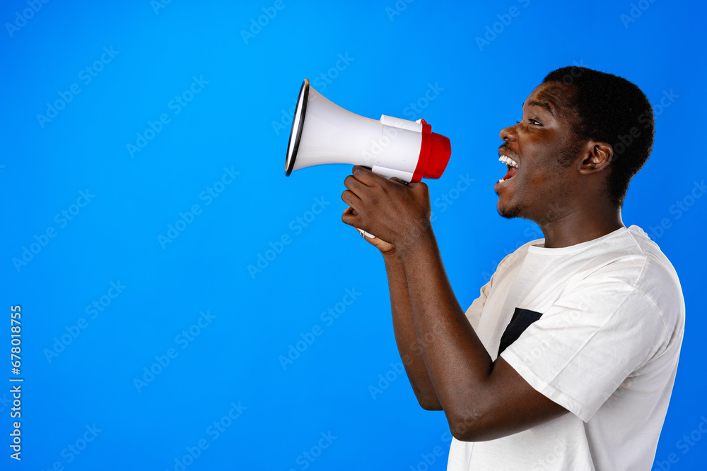 Positive african guy shouting with megaphone over blue background Positive african guy shouting with megaphone over blue background