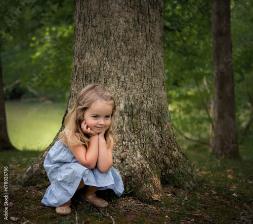 Beautiful little girl crouching with hands on cheeks outdoors photo