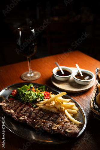 Strip roast with french fries and salad on wooden table with glass of red wine. Argentine restaurant concept. Gastronomy concept