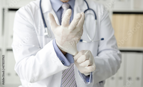 The doctor in the office puts on white protective gloves closeup