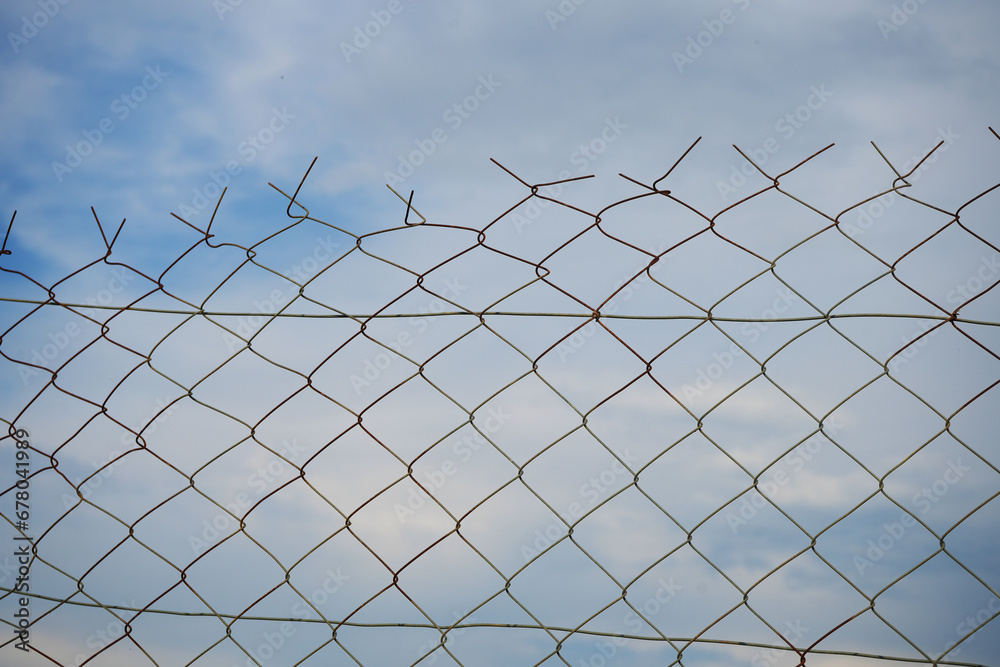 Looking up at a chain link fence with blue sky and clouds. wire fence. Chain link fence see sky. Opening in metallic fence. blue sky. Challenge. breakthrough concept. Looking up at a chain link fence with blue sky and clouds. wire fence. Chain link fence see sky. Opening in metallic fence. blue sky. Challenge. breakthrough concept.