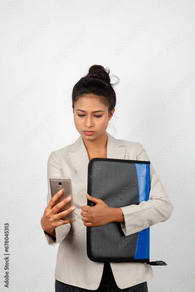 Cheerful corporate office lady holding a folder and a smartphone. Young woman in formal wear wearing white blazer against white background. Cheerful corporate office lady holding a folder and a smartphone. Young woman in formal wear wearing white blazer against white background.