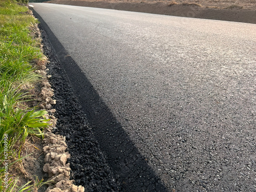 A close-up view of the hot and fresh asphalt layer on a newly constructed road, showing the texture and grain of the material and the equipment used for paving. construction and laying of the pavement
