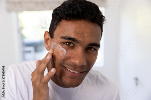 Happy biracial man applying face cream in bathroom at home