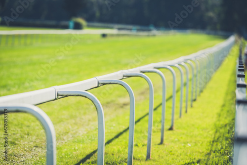 Empty horse race track with green grass and white fence