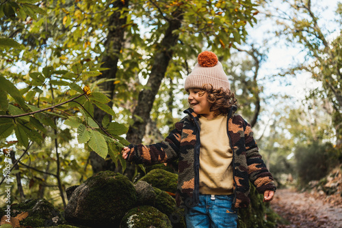 portrait of fashionable little boy with hat playing happily on a forest path while teaching his parents about plants