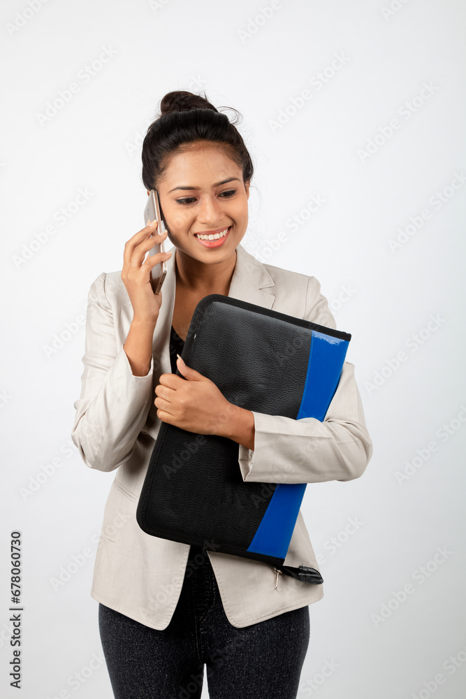 Cheerful corporate office lady holding a folder and a smartphone. Young woman in formal wear wearing white blazer against white background. Cheerful corporate office lady holding a folder and a smartphone. Young woman in formal wear wearing white blazer against white background.