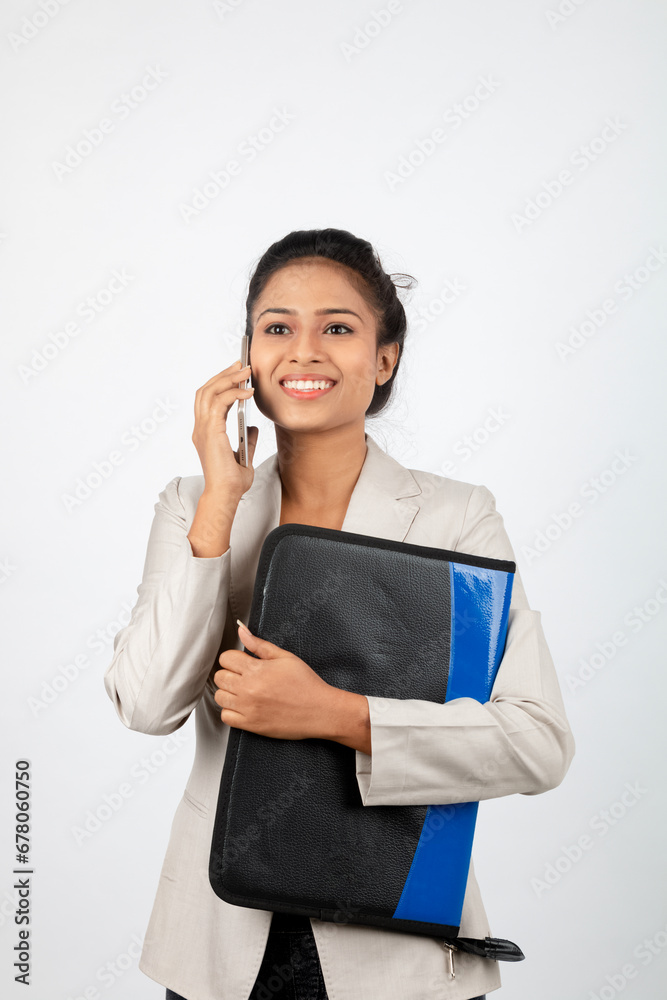 Cheerful corporate office lady holding a folder and a smartphone. Young woman in formal wear wearing white blazer against white background. Cheerful corporate office lady holding a folder and a smartphone. Young woman in formal wear wearing white blazer against white background.