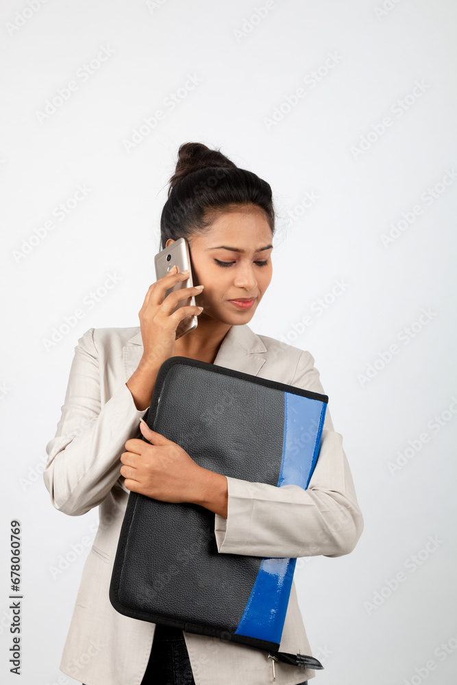 Cheerful corporate office lady holding a folder and a smartphone. Young woman in formal wear wearing white blazer against white background. Cheerful corporate office lady holding a folder and a smartphone. Young woman in formal wear wearing white blazer against white background.