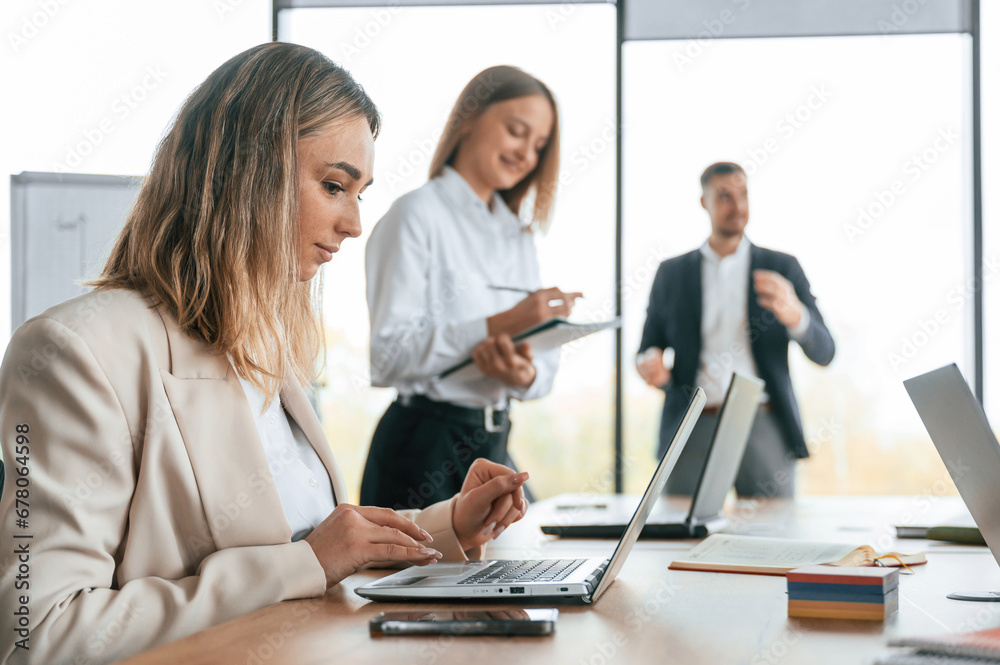 Using laptop that is on the table. Group of office workers are together indoors