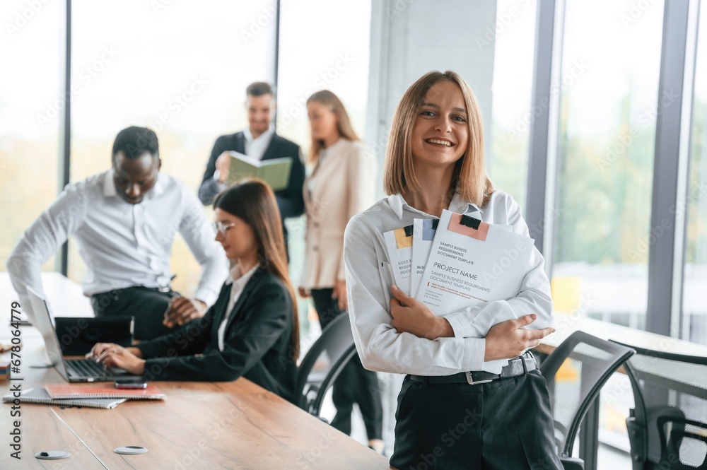 Happy woman is standing in front of her colleagues. Group of office workers are together indoors