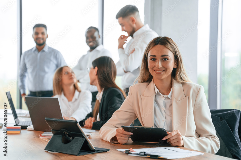 Woman is with notepad and tablet on table. Group of office workers are together indoors Woman is with notepad and tablet on table. Group of office workers are together indoors