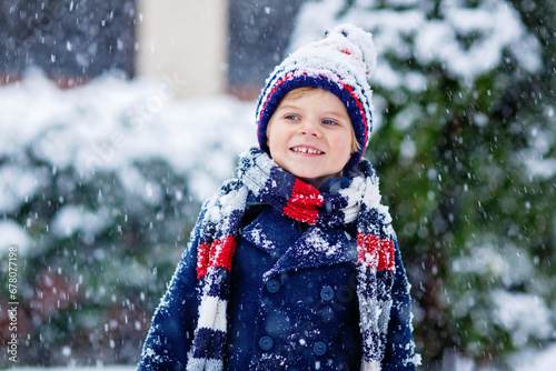Funny little kid boy in colorful clothes playing outdoors during strong snowfall