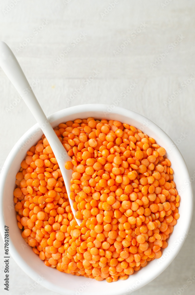 Orange lentils in a white bowl with a teaspoon on a light background. The concept of proper nutrition. Vegan and vegetarian food. Vertical orientation. Top view. Copy space. Orange lentils in a white bowl with a teaspoon on a light background. The concept of proper nutrition. Vegan and vegetarian food. Vertical orientation. Top view. Copy space.