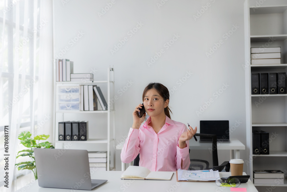 Young Asian woman, secretary, business consultant, sales manager talking on the phone in the office and business background, tax, accounting, statistics and analytical research concept. Young Asian woman, secretary, business consultant, sales manager talking on the phone in the office and business background, tax, accounting, statistics and analytical research concept.