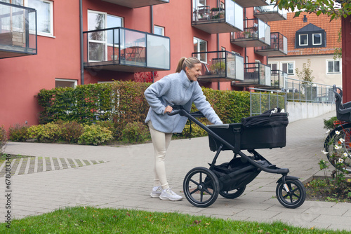 Mother with baby stroller walking outside modern apartmentbuildings in Sweden