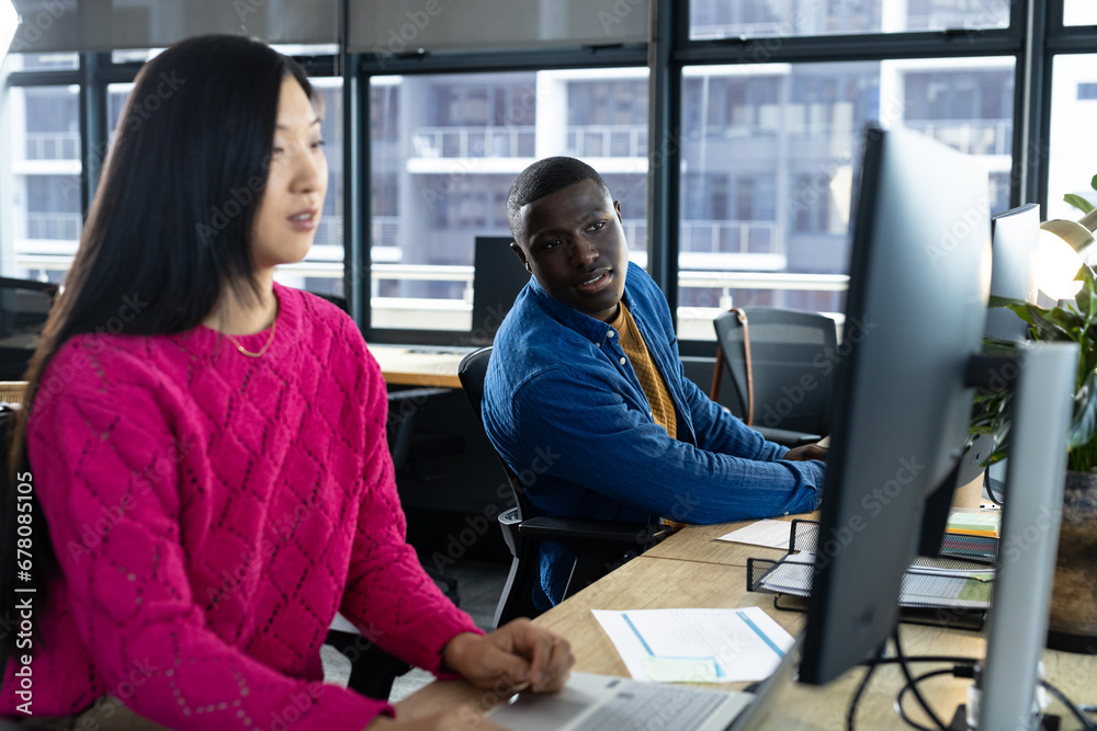 Busy diverse male and female colleague using computers at desks, talking in office Busy diverse male and female colleague using computers at desks, talking in office