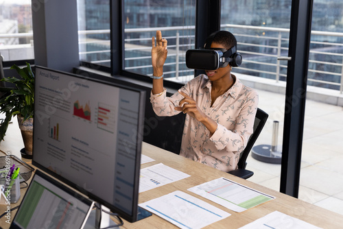 African american casual businesswoman wearing vr headset using virtual interface at desk in office photo
