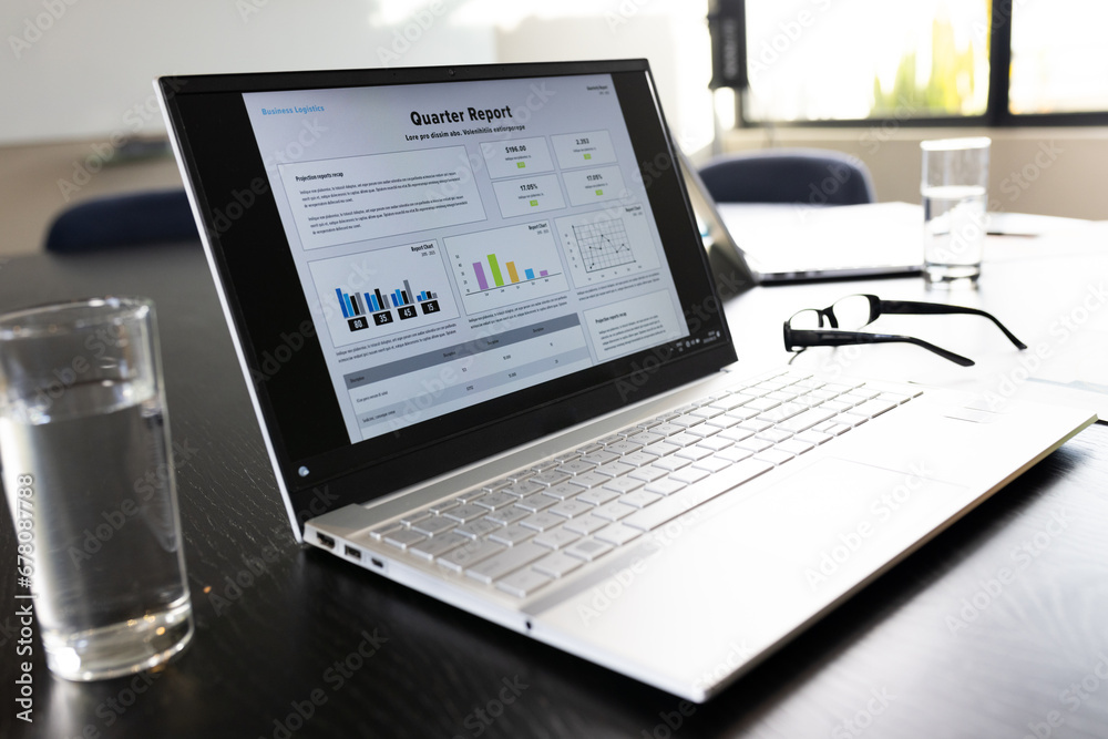 Laptop with quarter report text and graphs on screen on table in office meeting room Laptop with quarter report text and graphs on screen on table in office meeting room