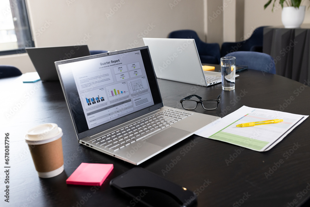 Takeaway coffee, laptop with quarter report on screen and documents on table in office meeting room Takeaway coffee, laptop with quarter report on screen and documents on table in office meeting room