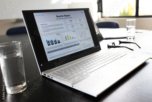 Laptop with quarter report text and graphs on screen on table in office meeting room photo