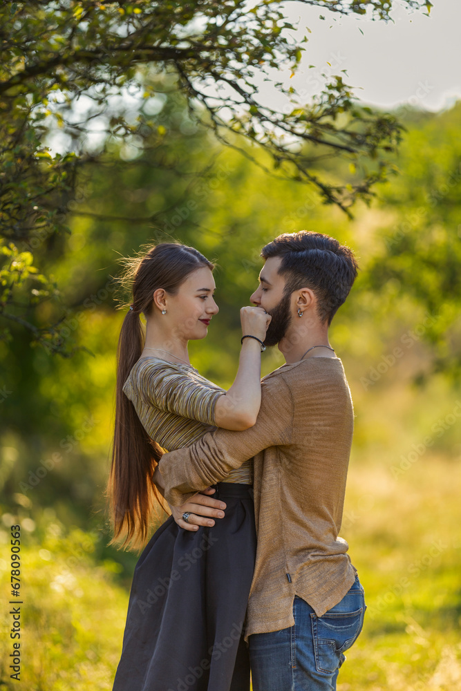 Fototapeta premium young couple, illuminated by the backlit sun, hugging in nature
